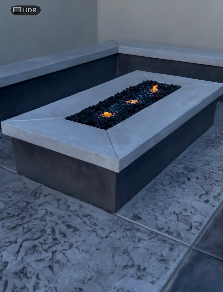 Modern concrete fire pit with black fire glass on a stamped concrete patio
