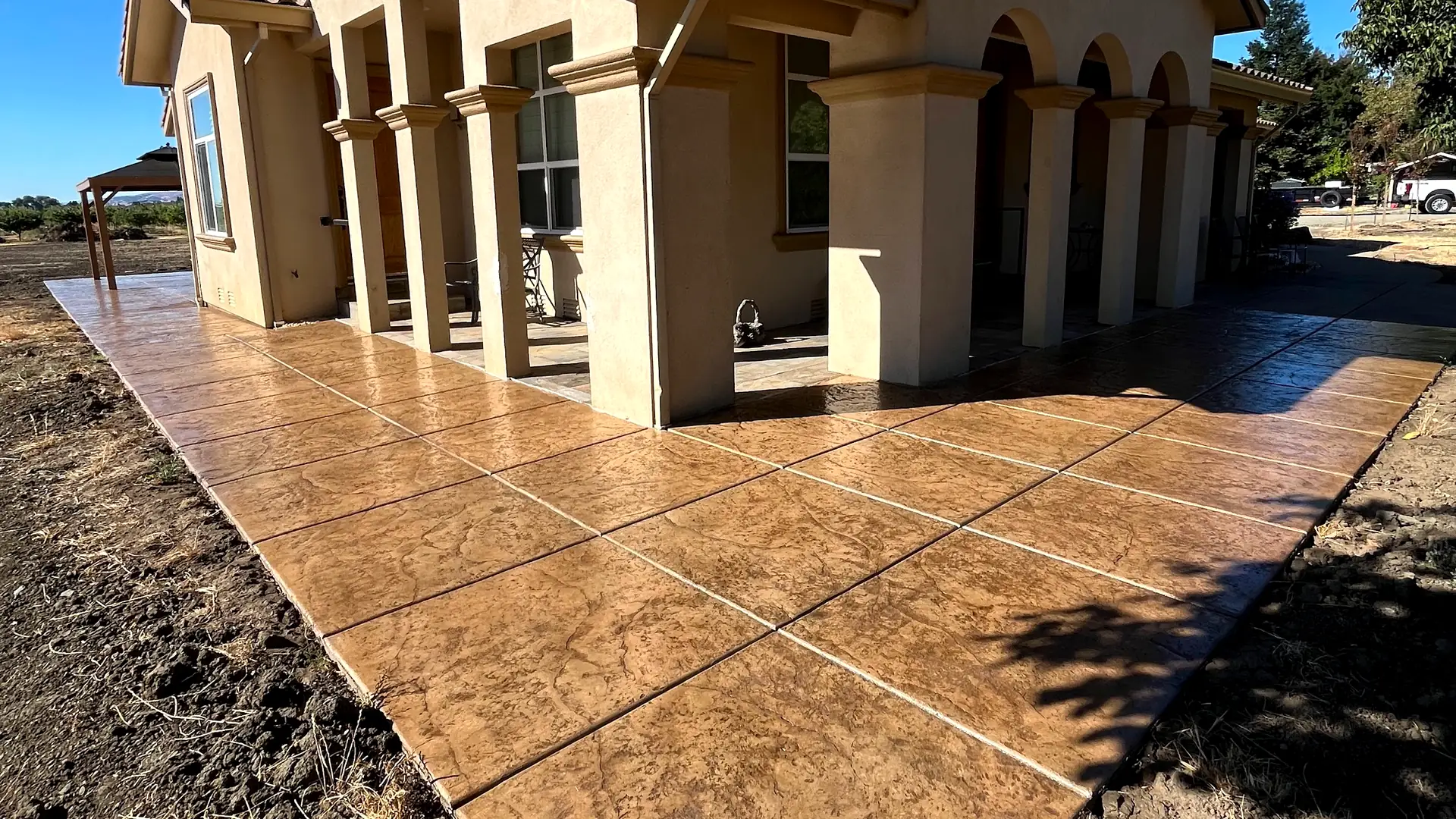 Tan ashlar-pattern stamped concrete wraparound patio with white colonnade